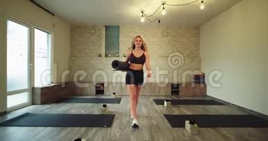 穿着舒适的运动服，在健康瑜伽工作室进行瑜伽训练后，快乐的女士带着运动垫散步